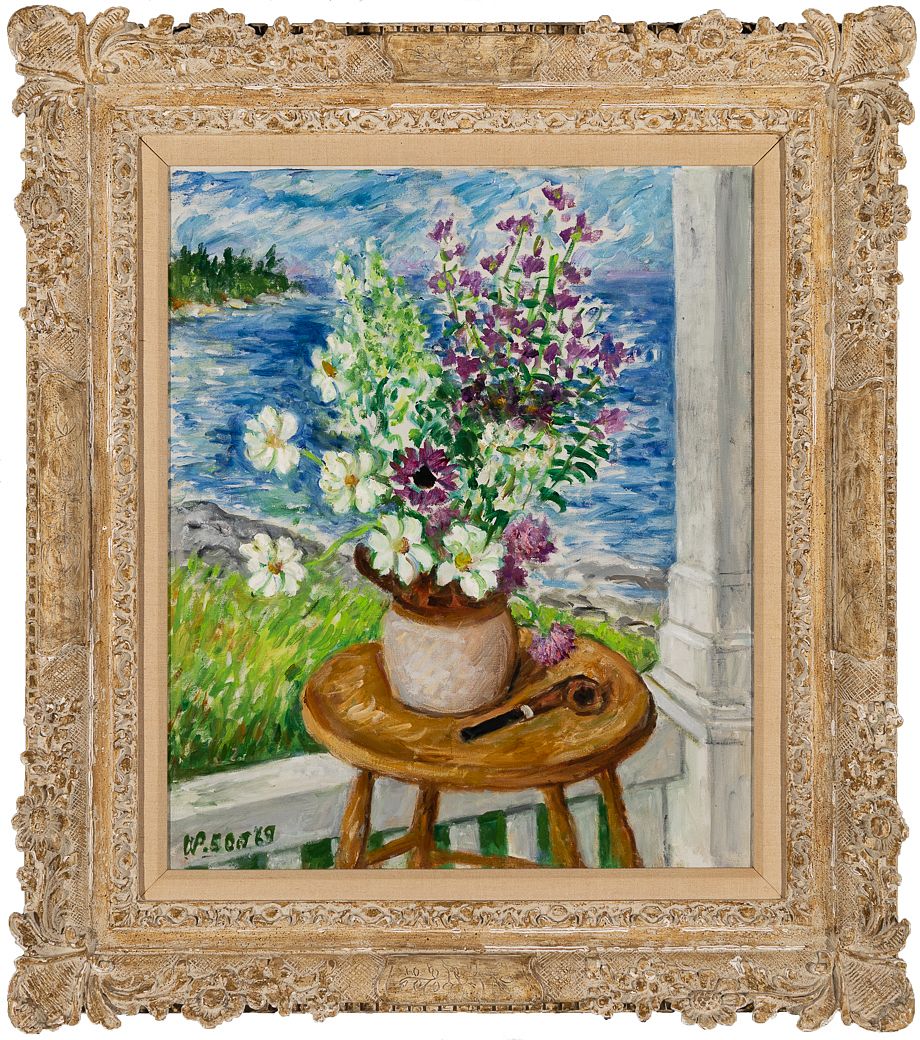A colourful painting of white and purple flowers in a pale vase on a round wooden table, with a pipe beside it and blue water and a green shoreline beyond, is shown within an ornate cream-and-gold carved frame. A dark painted signature and date are visible at the lower left of the composition.
