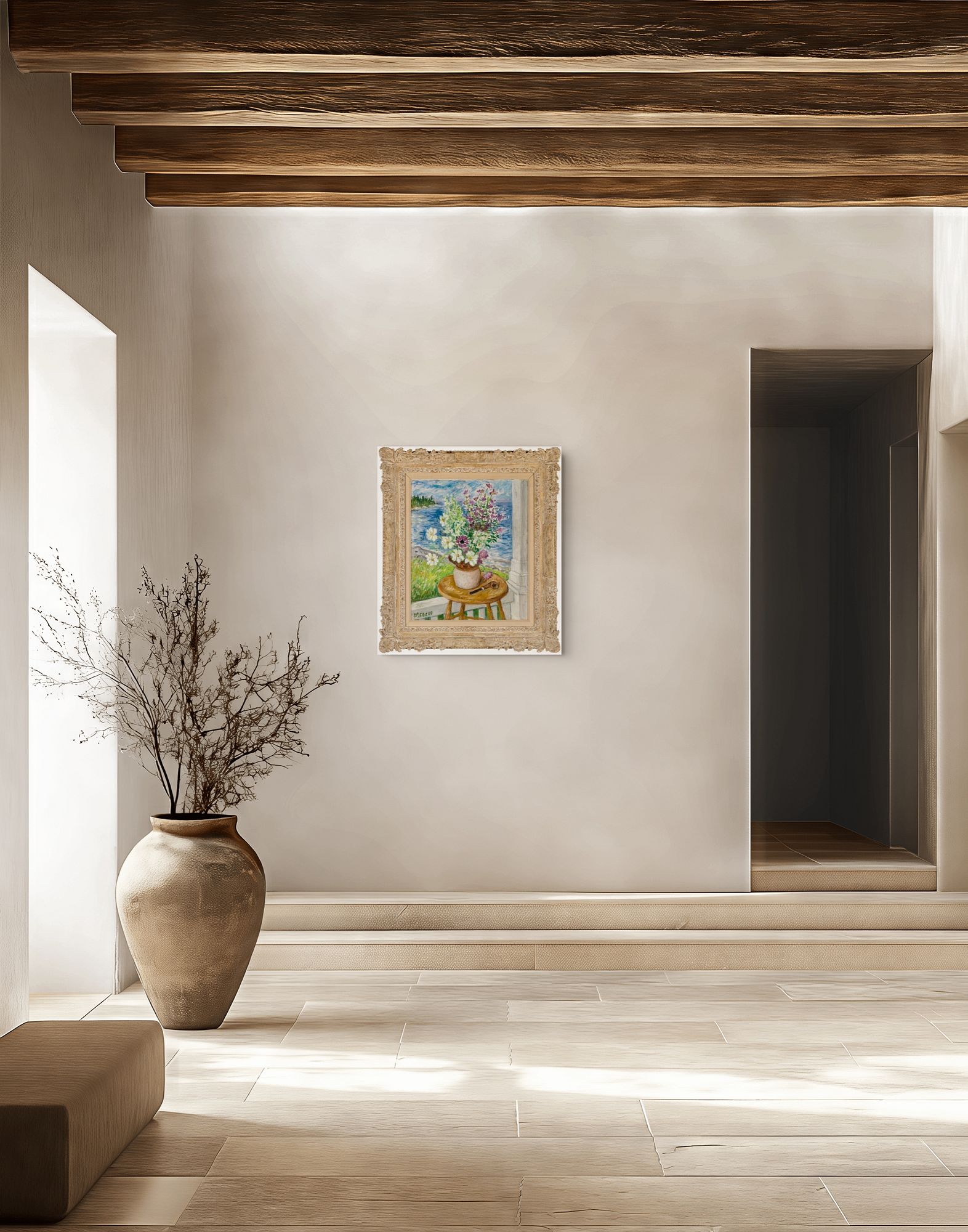 A small, ornate cream-framed painting of flowers in a vase on a round table hangs on a pale wall in a sunlit interior. Exposed dark wooden ceiling beams, a large ceramic vessel holding bare branches, and a recessed doorway surround the work; a small inscription is visible at the painting’s lower left but cannot be read clearly.